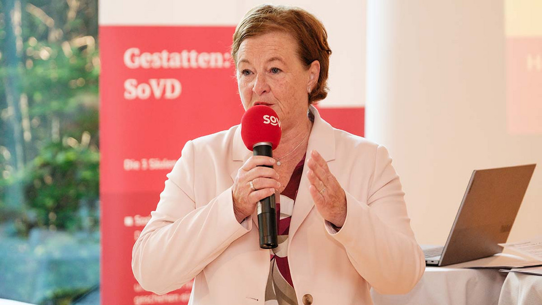Eine Frau steht im Raum und spricht in ein SoVD-Mikrofon. 
