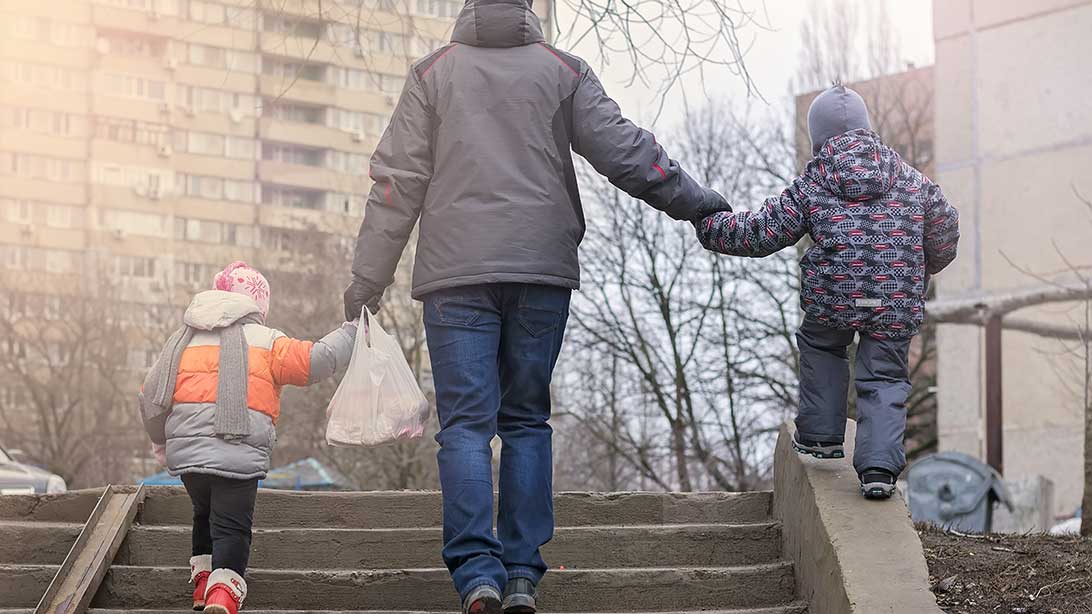 Erwachsener mit zwei Kindern in einer Plattenbausiedlung. 